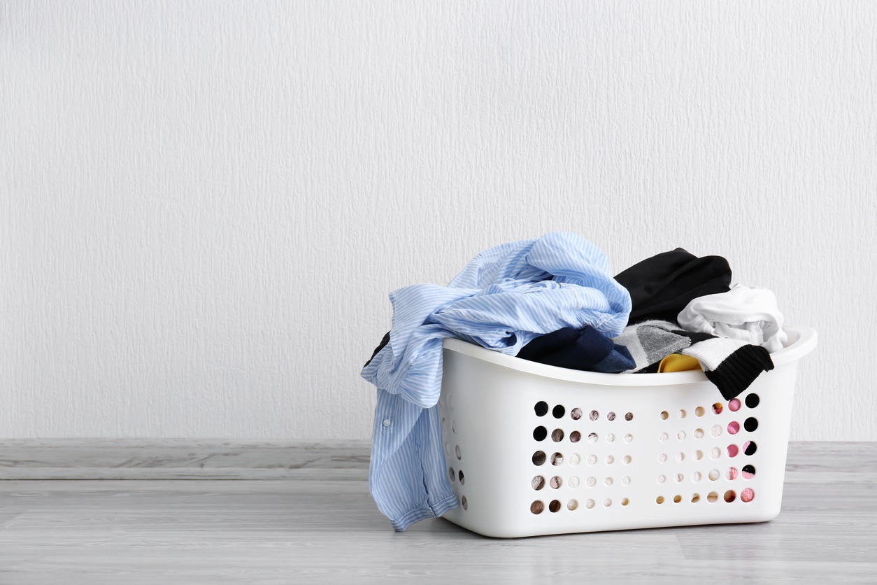 Basket with dirty laundry on floor against light wall